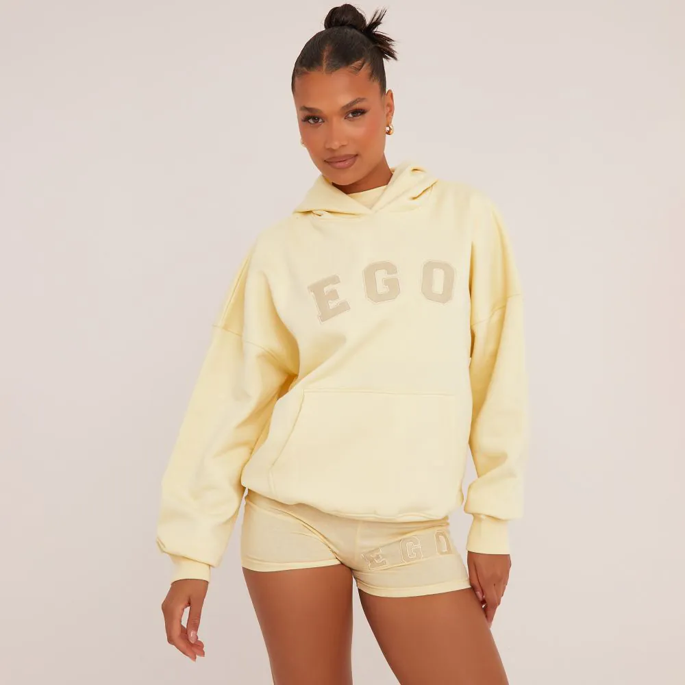 An oversized yellow hoodie with an 'Ego' slogan graphic on the front. The model is wearing with the matching yellow micro shorts. 